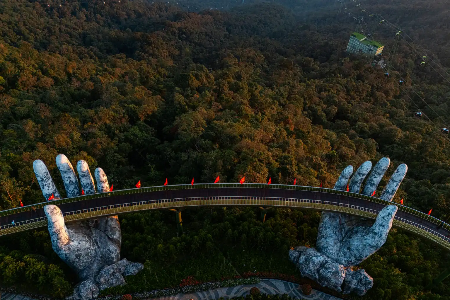 Aerial view of the Golden Bridge held by two stone hands above green forest