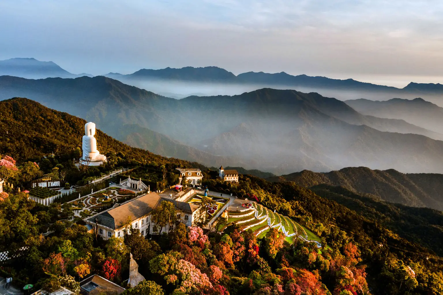 Aerial view of misty mountain ridges and a white Buddha statue over Ba Na Hills at sunrise