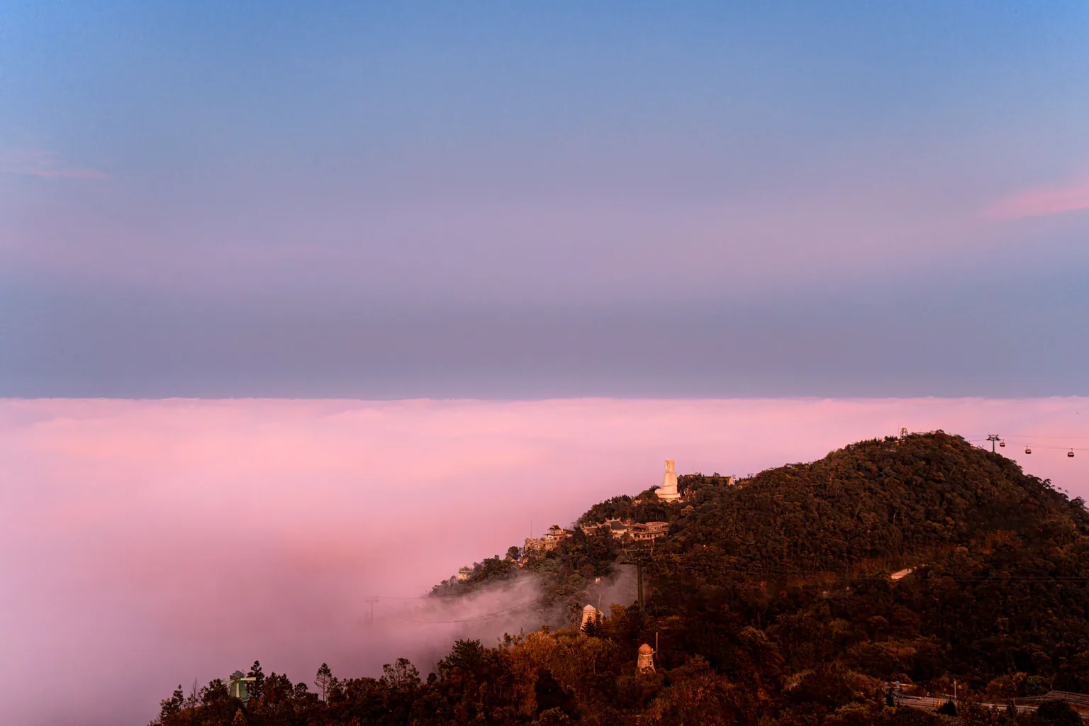 A hilltop rising from a pink sea of clouds at sunset on Ba Na Hills