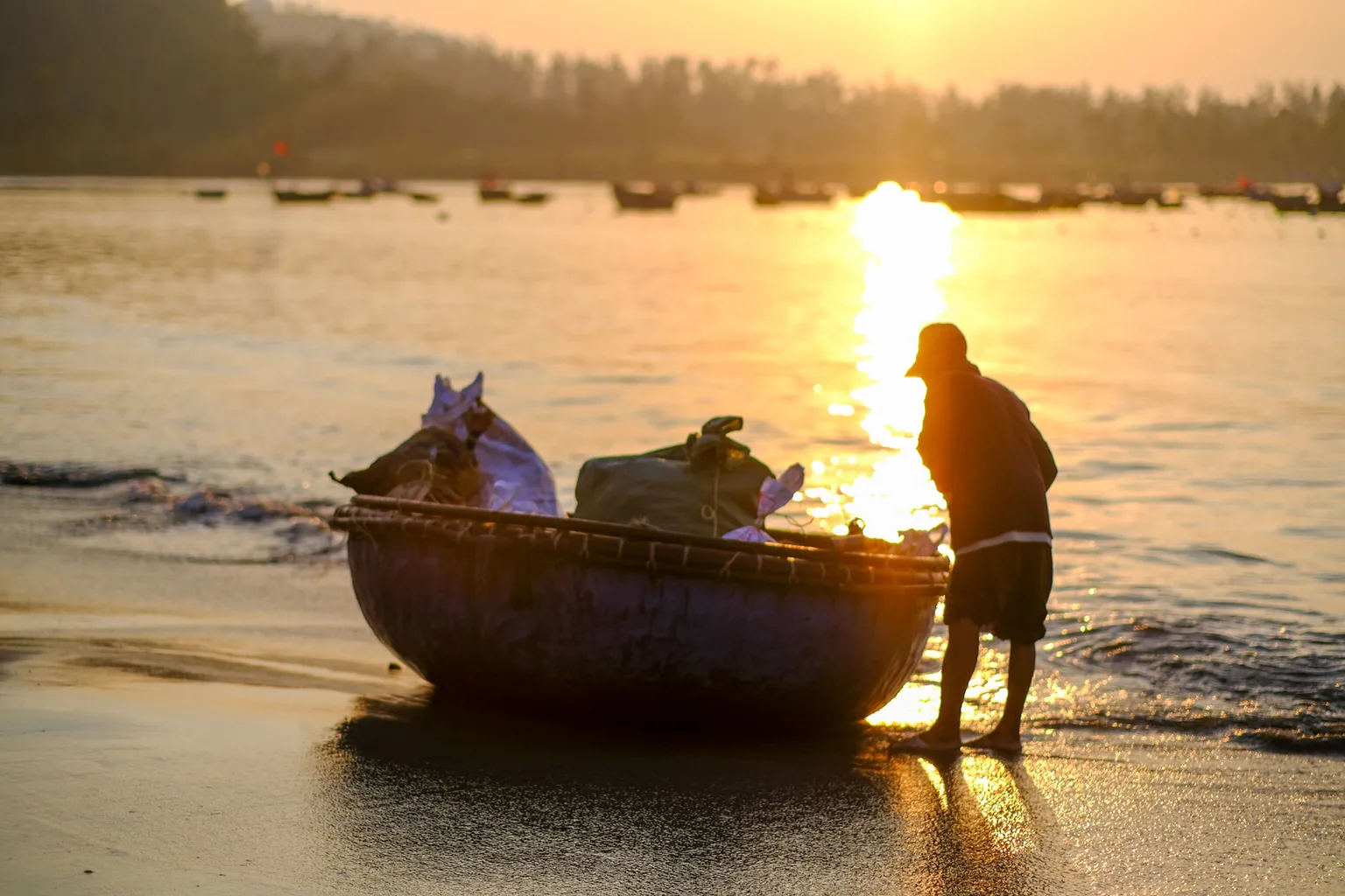 A fisherman beside a round basket boat on a Da Nang beach at golden sunrise