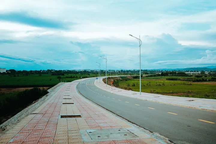 Cung đường rộng đi qua đồng ruộng xanh dưới bầu trời nhiều mây