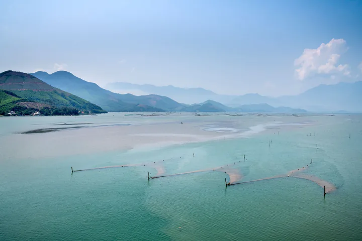 Fishing stakes and nets with the Bach Ma range reflected in the misty Lap An Lagoon