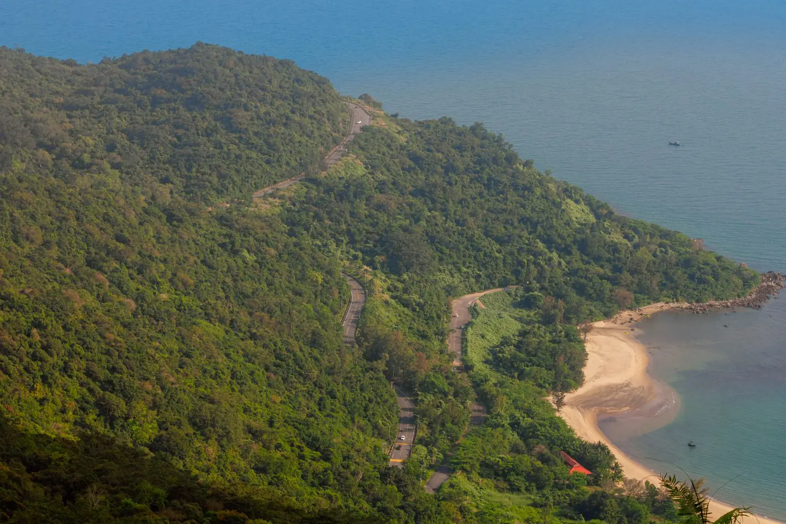 沿着长满绿树的山坡蜿蜒的道路，俯瞰沙滩和大海