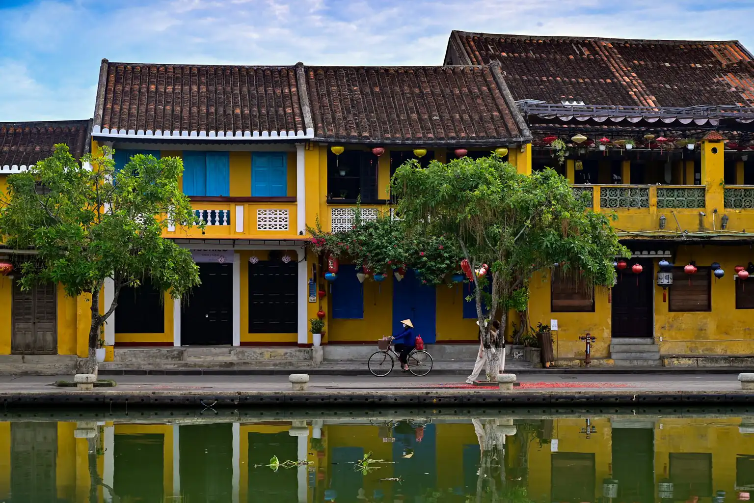 Yellow old-town houses reflected in a canal in Hoi An with a cyclist in the distance