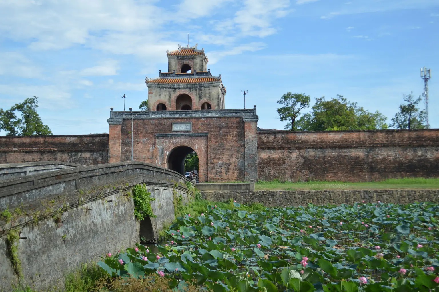 A historic citadel gate beside a lotus pond and a stone bridge in Hue