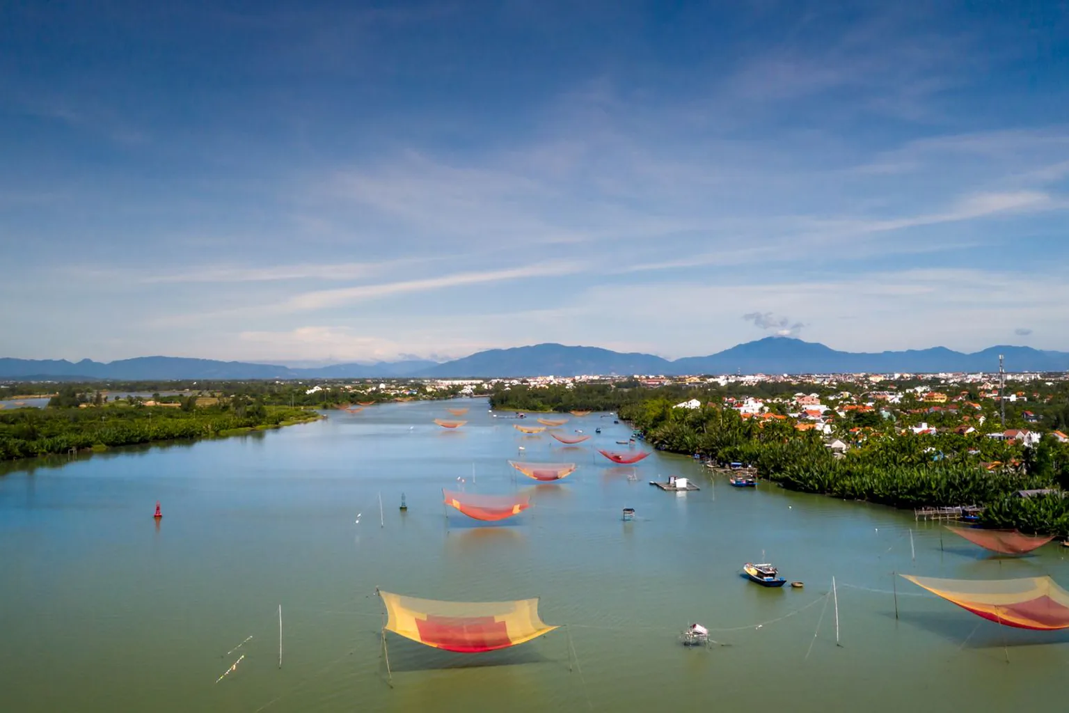 Red fishing nets spread over a calm river with mountains in the distance