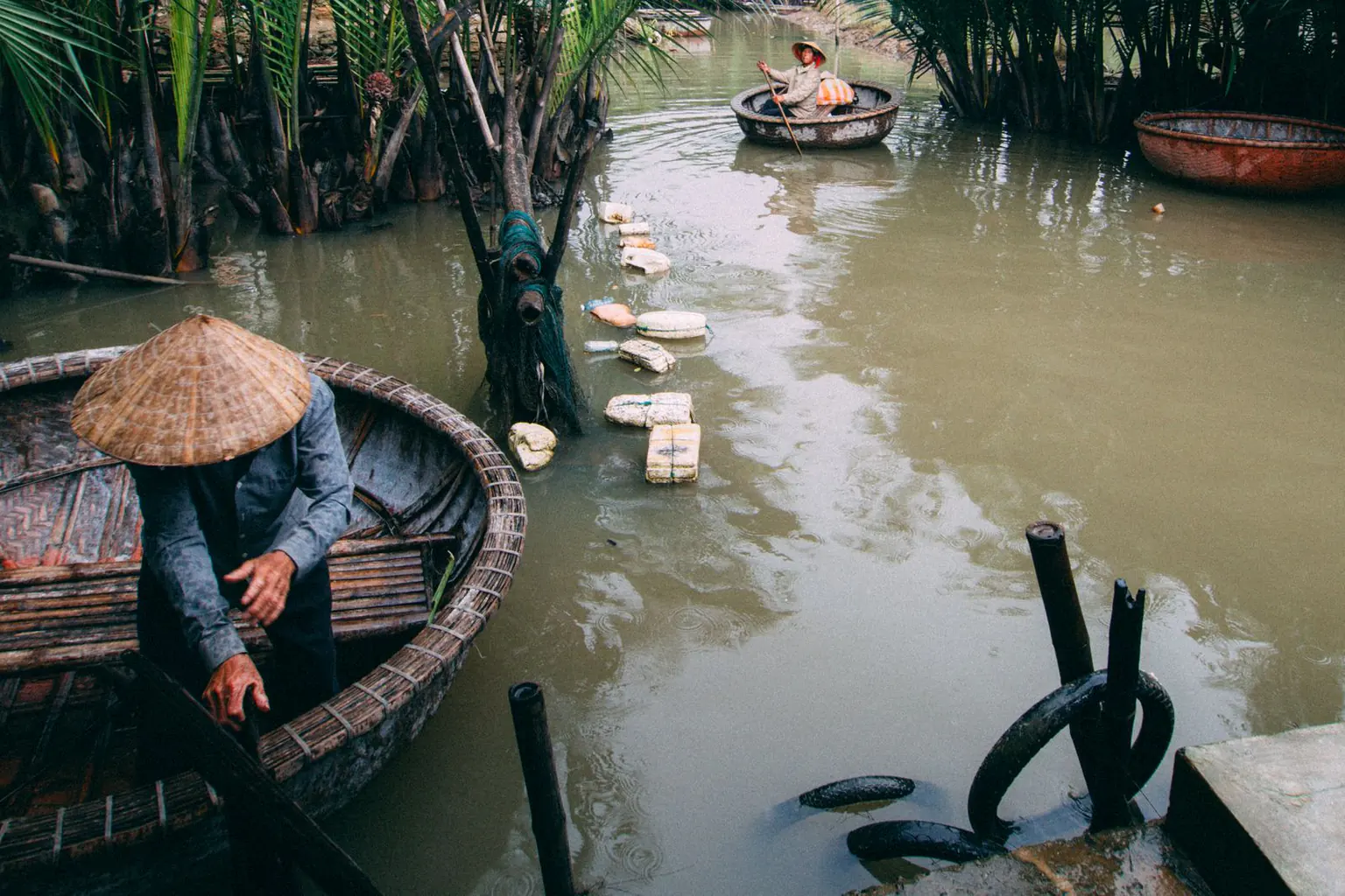 Basket boats moving along a green coconut-lined canal
