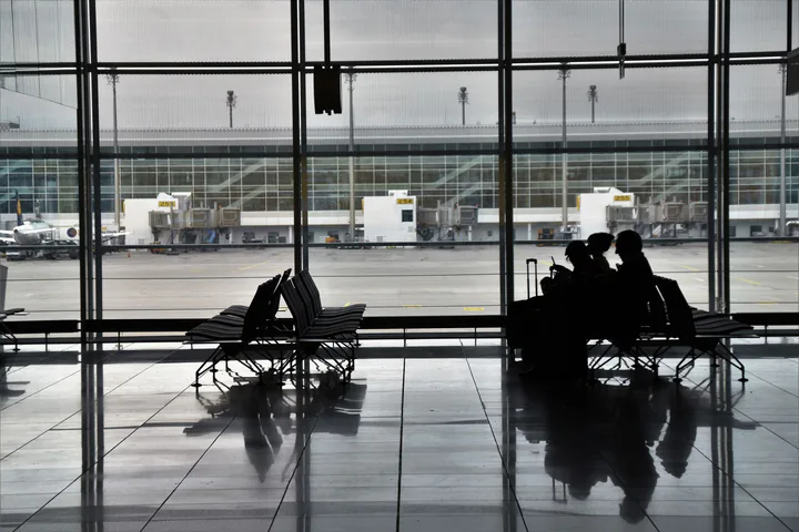 International travellers looking at the runway through a glass wall in a modern waiting hall