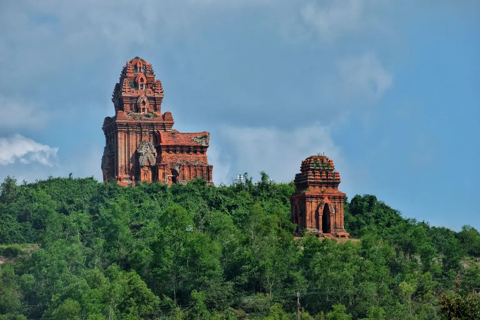 Red-brick Cham towers on a forested hill under a blue sky