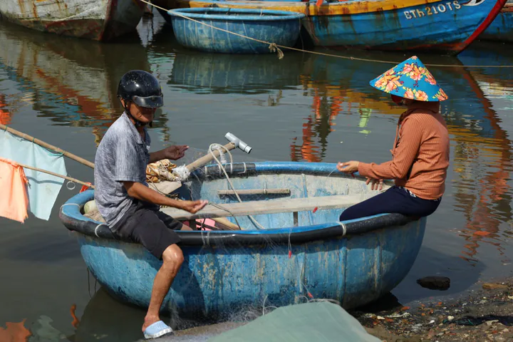 Hai người làm việc trên thuyền thúng giữa mặt nước yên