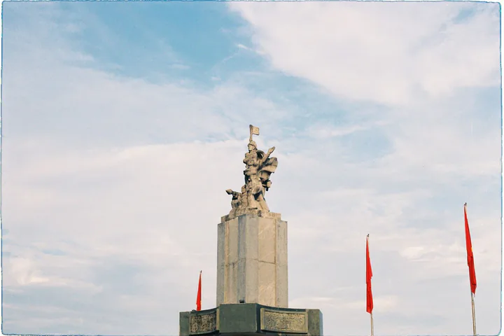 Tượng đài cao với những lá cờ đỏ dưới bầu trời xanh